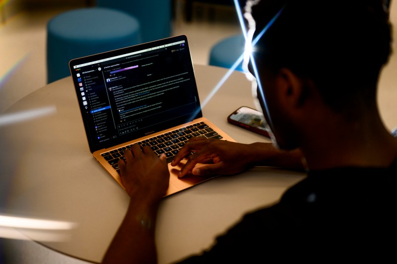 David Alade typing a message on Slack on his laptop.