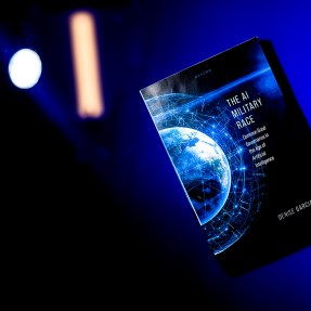 A blue and black-colored book titled "The AI Military Race" is suspended in the air in front of a blue background.