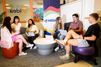 People sitting in a group with laptops in front of a MOSAIC banner.