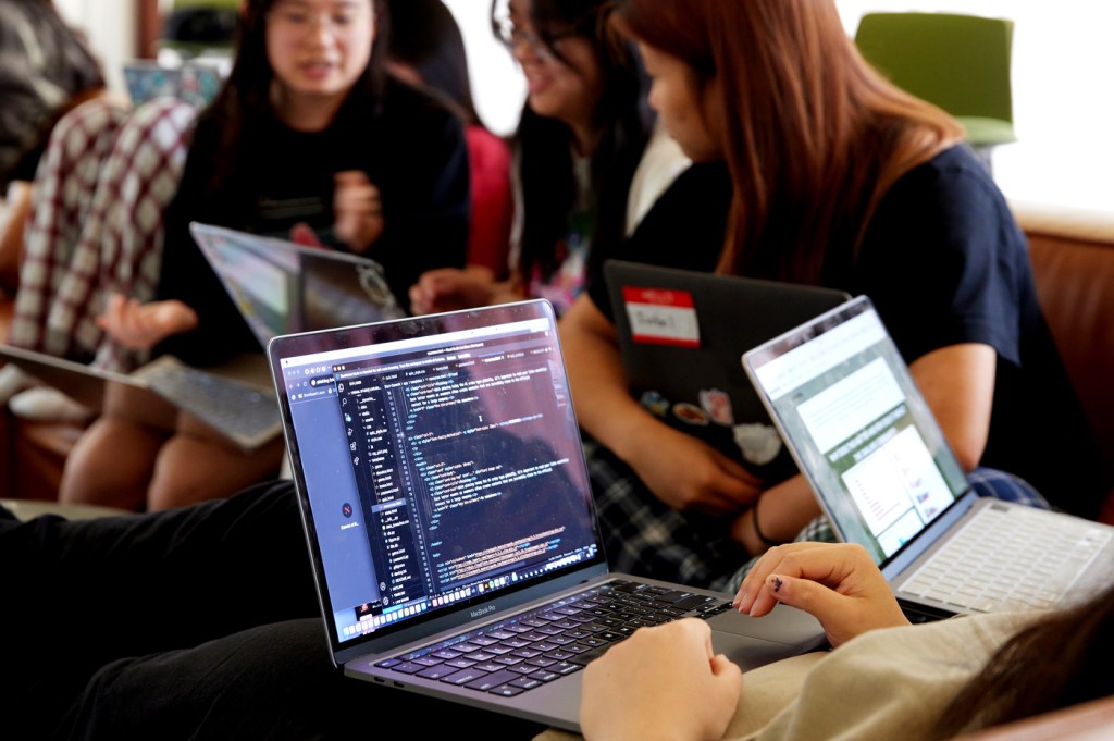 Students typing lines of code on their laptops.