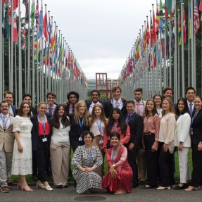 Group of students posing for a photo outside in Geneva in between rows of flag poles.