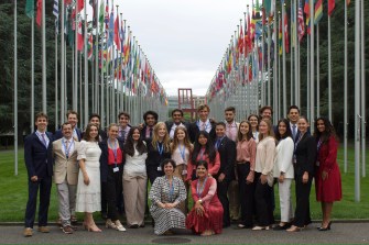 Group of students posing for a photo outside in Geneva in between rows of flag poles.