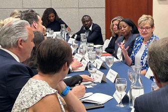 Multiple people sit around a large, blue-covered table at the United Nations Environment Assembly to discuss plastic pollution solutions.