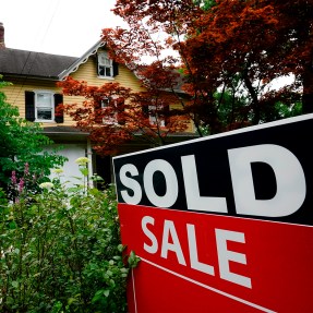 A "sold" sale sign outside of a yellow house.