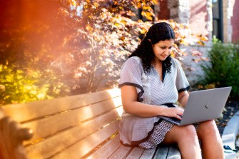 Person sitting on a park bench using their laptop.