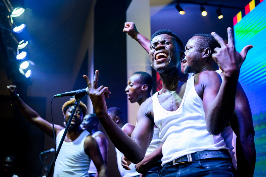 Akoo Show Choir members singing on stage in front of a microphone.