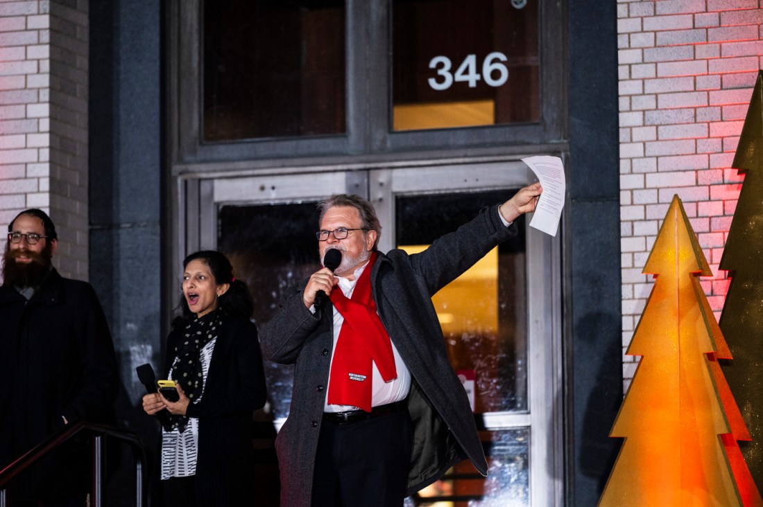 A person talks into a microphone outside Northeastern's Joy and Light Holiday Showcase.