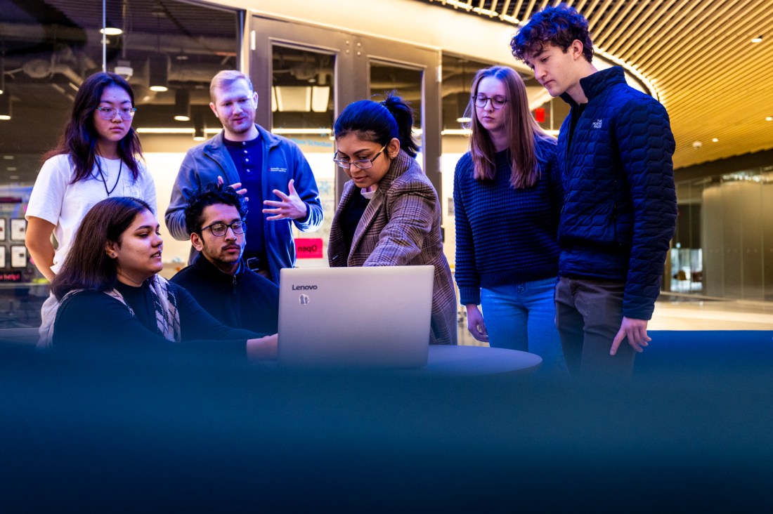 Srirupa Chakraborty gestures to a laptop screen while her students hover around looking over her shoulders. 