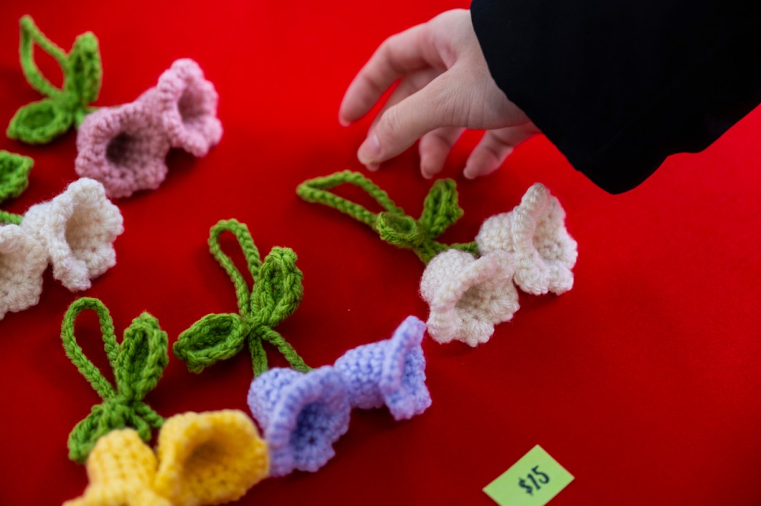 Hand reaching for crocheted flowers on a red background.