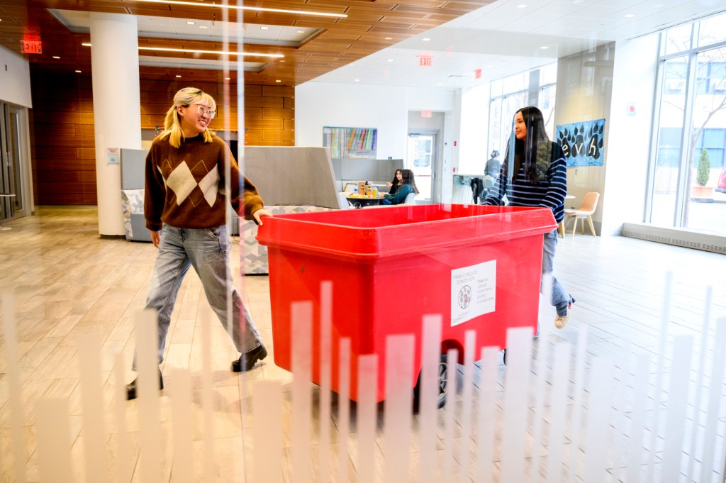 Kari Du and Amy Tey wheeling a red Trash2Treasure bin in East Village.