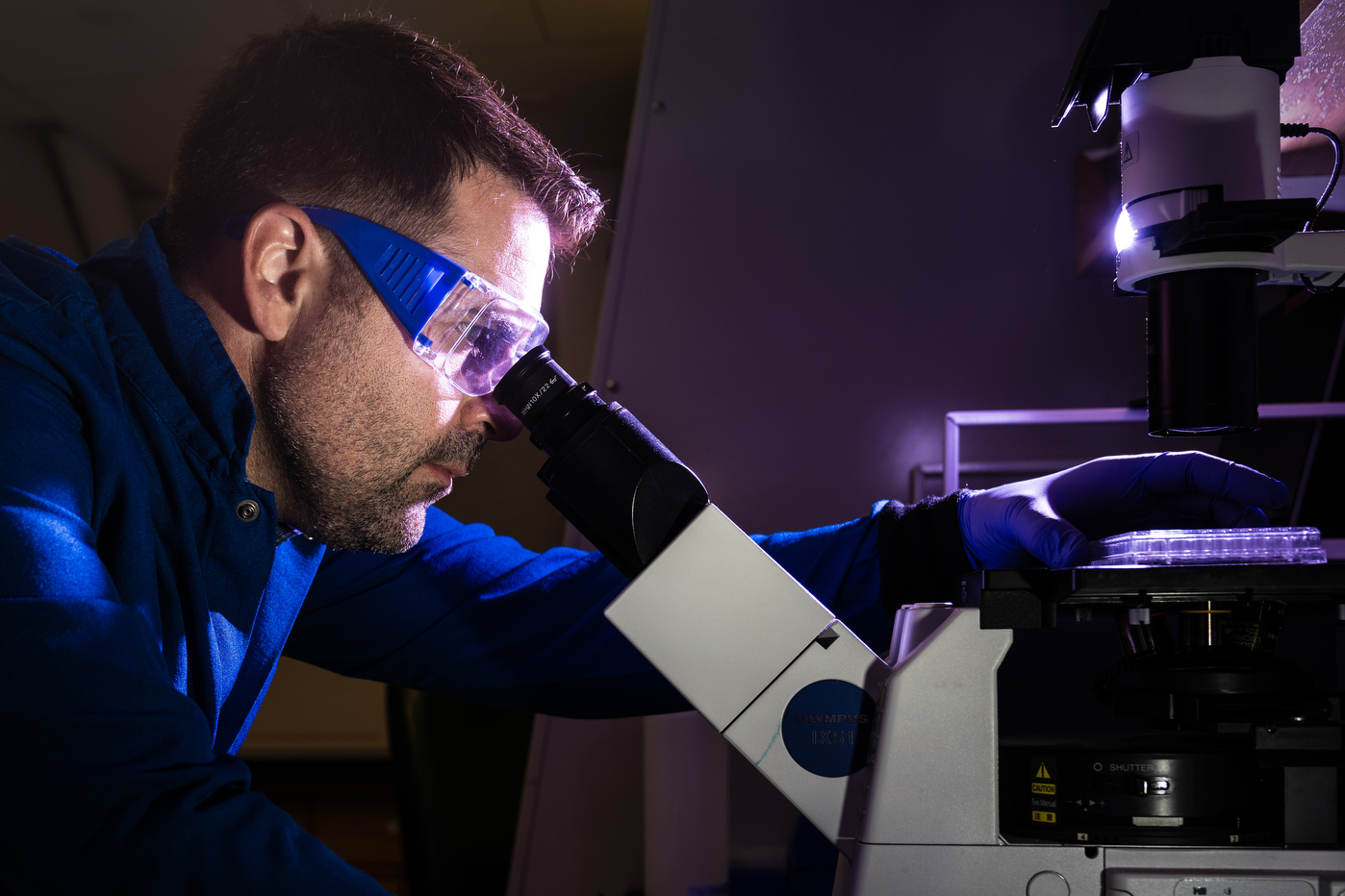 Stephen Hatfield looking in a micrscope in a dark lab room.