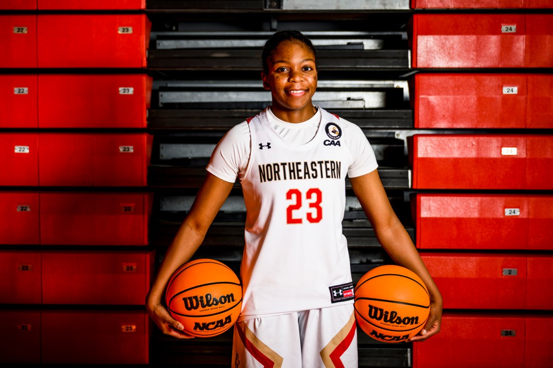 Gemima Motema in Northeastern basketball gear holding two basketballs.