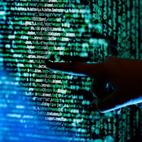Hand pointing to lines of code on a black screen.