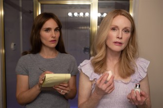 Screen capture from the film May December of Julianne Moore and Natalie Portman both standing looking in a mirror while doing their makeup.