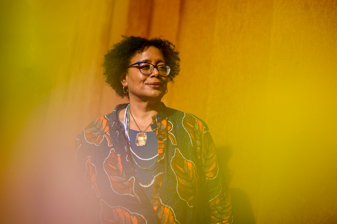 Headshot of Northeastern community member wearing a blue shirt, large gold necklace, and a flowy blue shirt with red leave prints on it. 