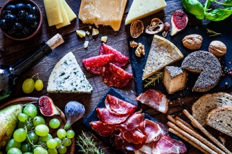 A rustic wooden table topped with cheese, grapes, and cured meats.