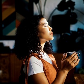 Person holding a cup of coffee with their eyes shut.