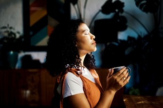 Person holding a cup of coffee with their eyes shut.