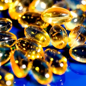 Yellow tinted oblong vitamin D pills on a blue surface.