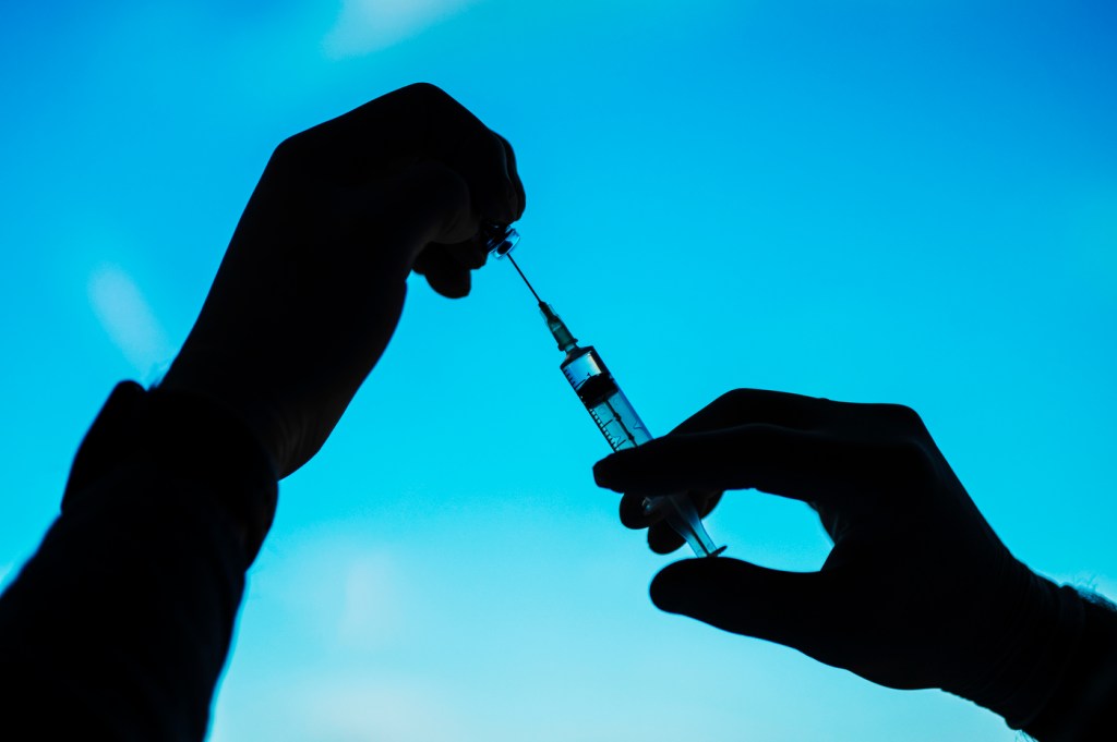 Silhouette of a person's hands filling a vaccine syringe.