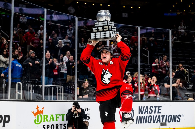 Northeastern women's hockey team member holding the Beanpot trophy up in the air.