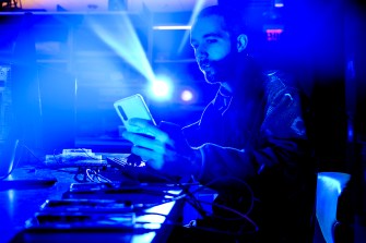 A person holds a cell phone inside a brightly lit blue-colored room.