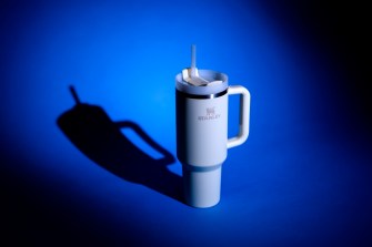 A white stanley cup on a blue background lit up by studio photo lights.