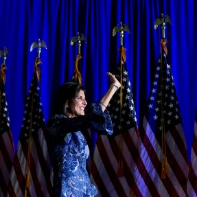 Nikki Haley standing in front of a row of US flags waving to a crowd off-camera.