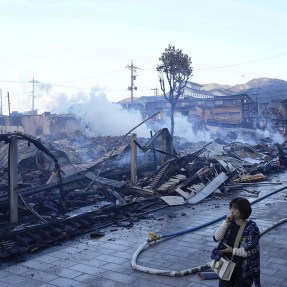 People walk past a burn-out marketplace following an earthquake in Japan.