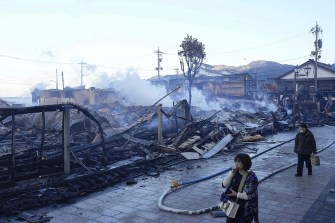 People walk past a burn-out marketplace following an earthquake in Japan.