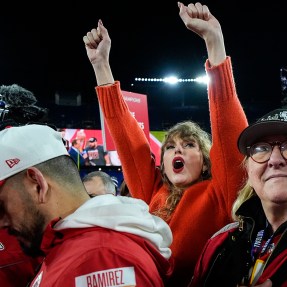 Taylor Swift cheering with her arms up while standing next to Donna Kelce watching the Kansas City Chiefs receive a trophy.