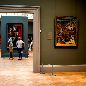 Two people look at art inside a museum with green-colored walls.