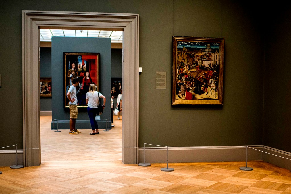 Two people look at art inside a museum with green-colored walls.