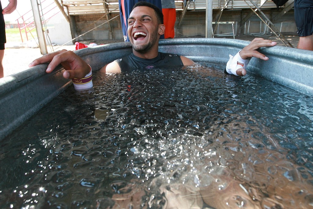 A person wearing a black shirt sits inside an ice bath.