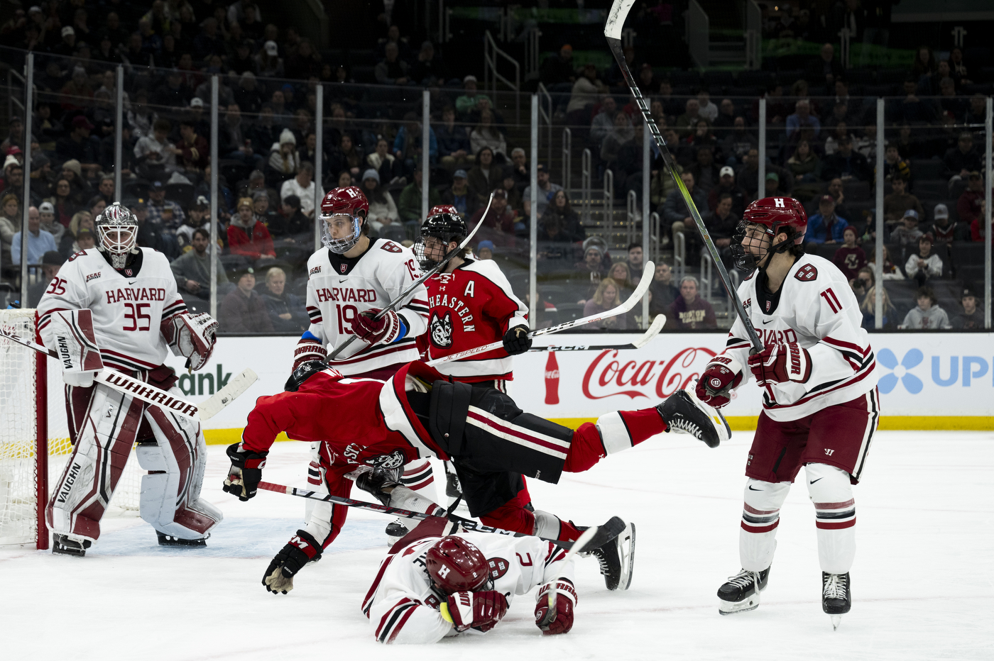 Northeastern hockey players clashing in front of Harvard's net.