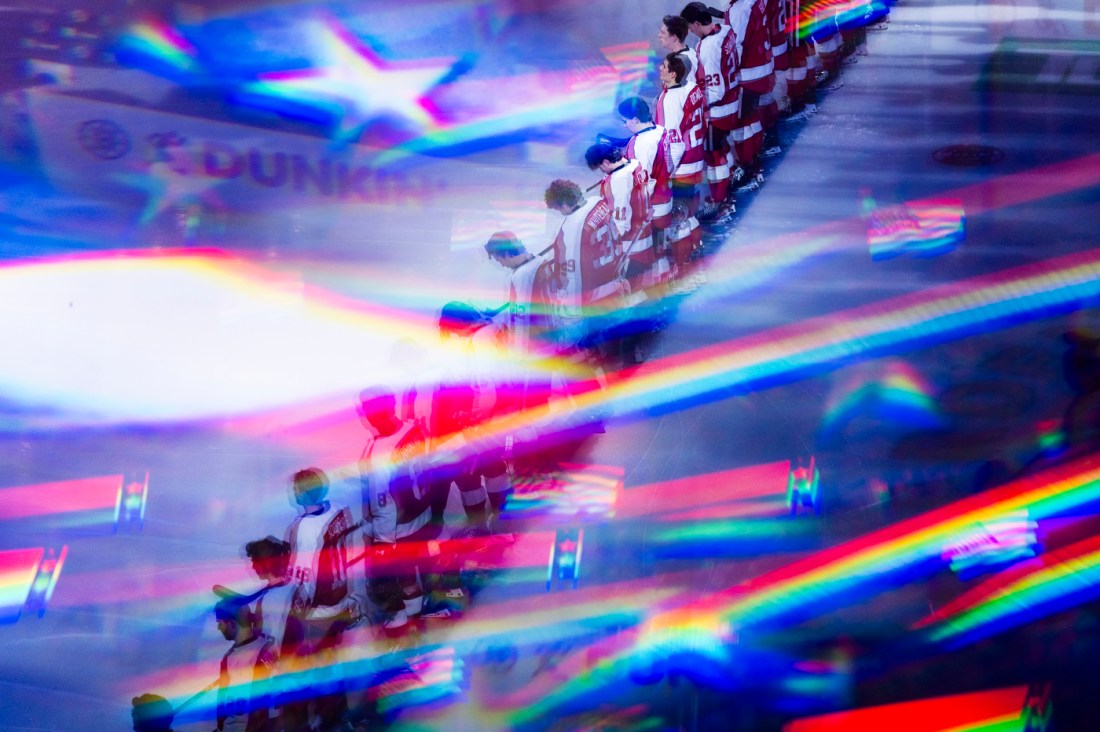 The men's hockey team lined up before the start of the game, overlayed by the American flag.