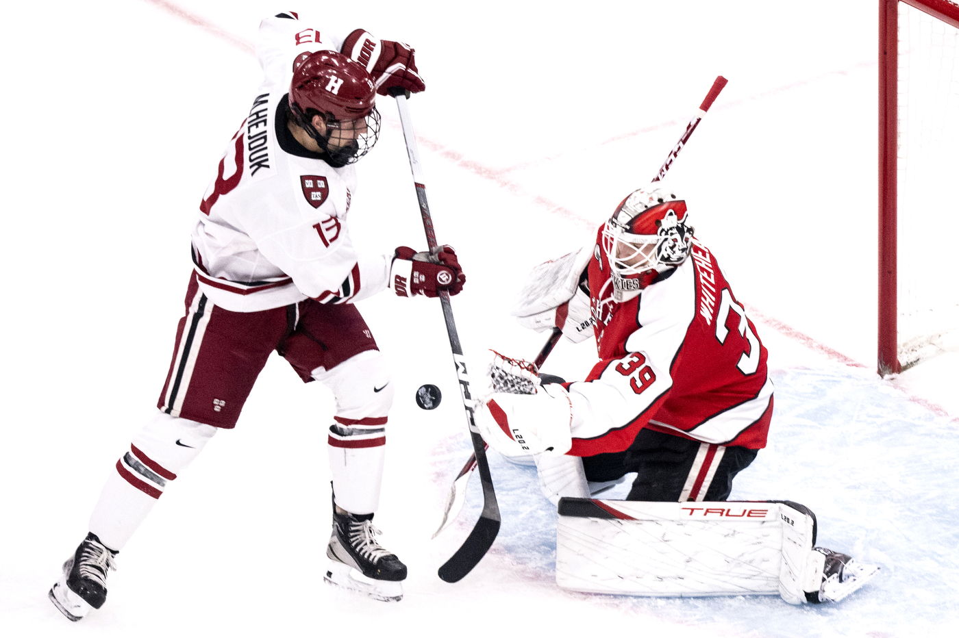 Northeastern men's hockey goalkeeper saving a shot by a Harvard player.