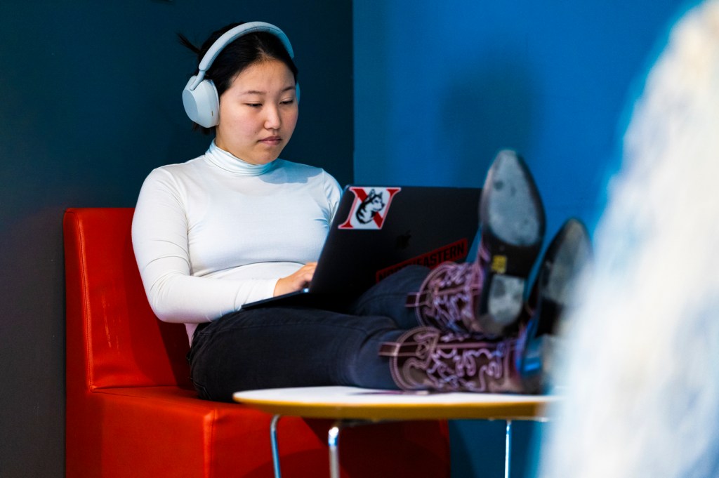 A person wearing purple-colored cowboy boots works on their laptop while sitting on a bright red chair.