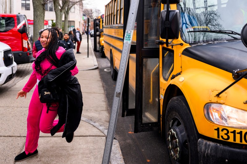 Kids walking off of a yellow school bus. 