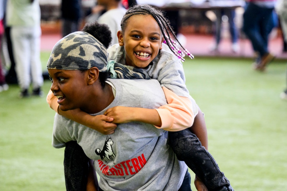 Two kids, one on the other's back, smiling and laughing.