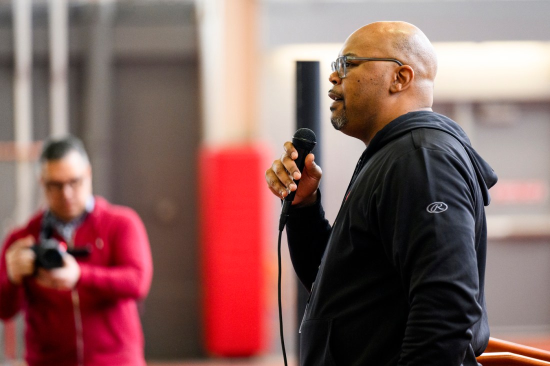 A person wearing a black hoodie speaking into a microphone.