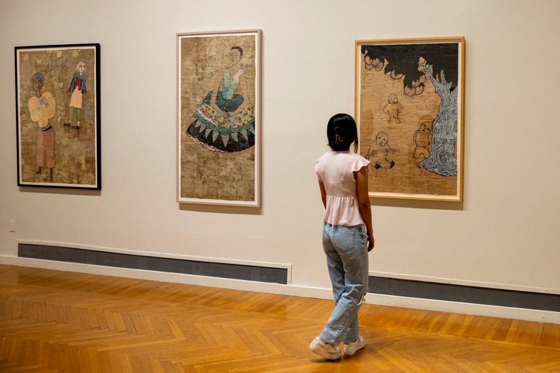 A person working at a painting next two others on a wall in an art gallery.