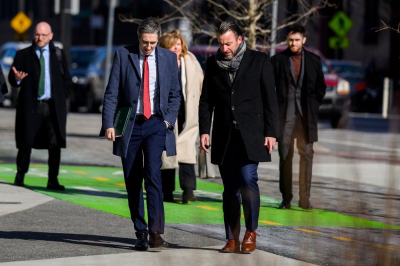 Multiple people in suits walk outside on a sunny day.