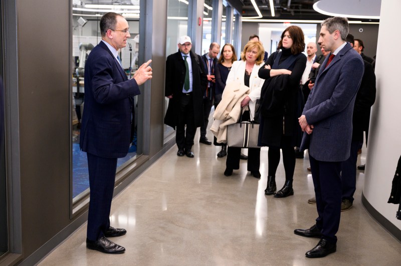 People in suits stand around a tour guide inside a brightly lit building.