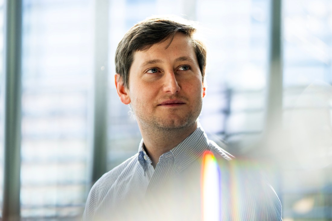 Headshot of Joshua Curtiss, wearing a button-down shirt inside a glass building.