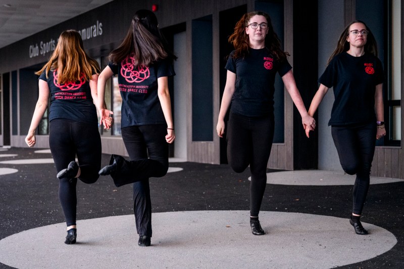 Four Northeastern’s Irish Dance Club members dance together in a line outside.