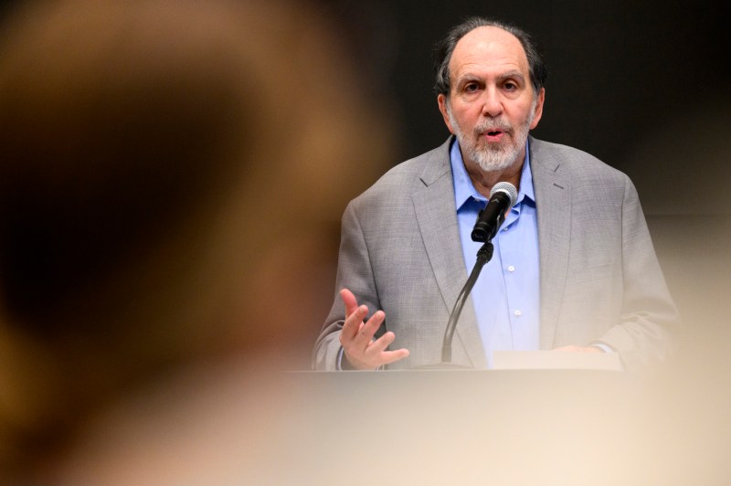 Person wearing grey suit jacket and blue shirt speaking into a microphone.