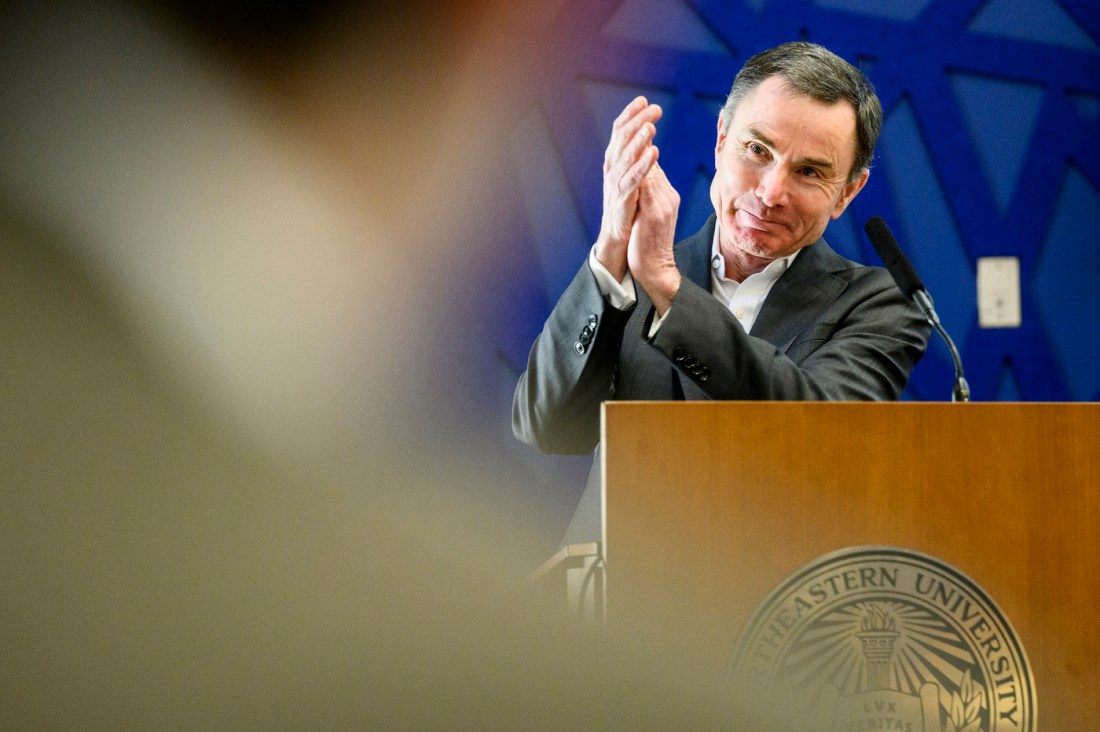 David Madigan, the Provost and Senior Vice President for Academic Affairs, claps at a podium in front of a blue-colored background.