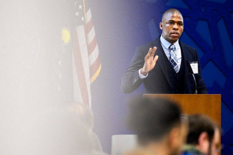 Rashad Cope, Deputy Chief of Worker Empowerment, City of Boston, speaks at a podium in front of a blue-colored background about the benefits of Boston's youth employment program.