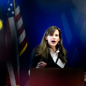 Alicia Modestino speaks at a podium in front of a blue background.